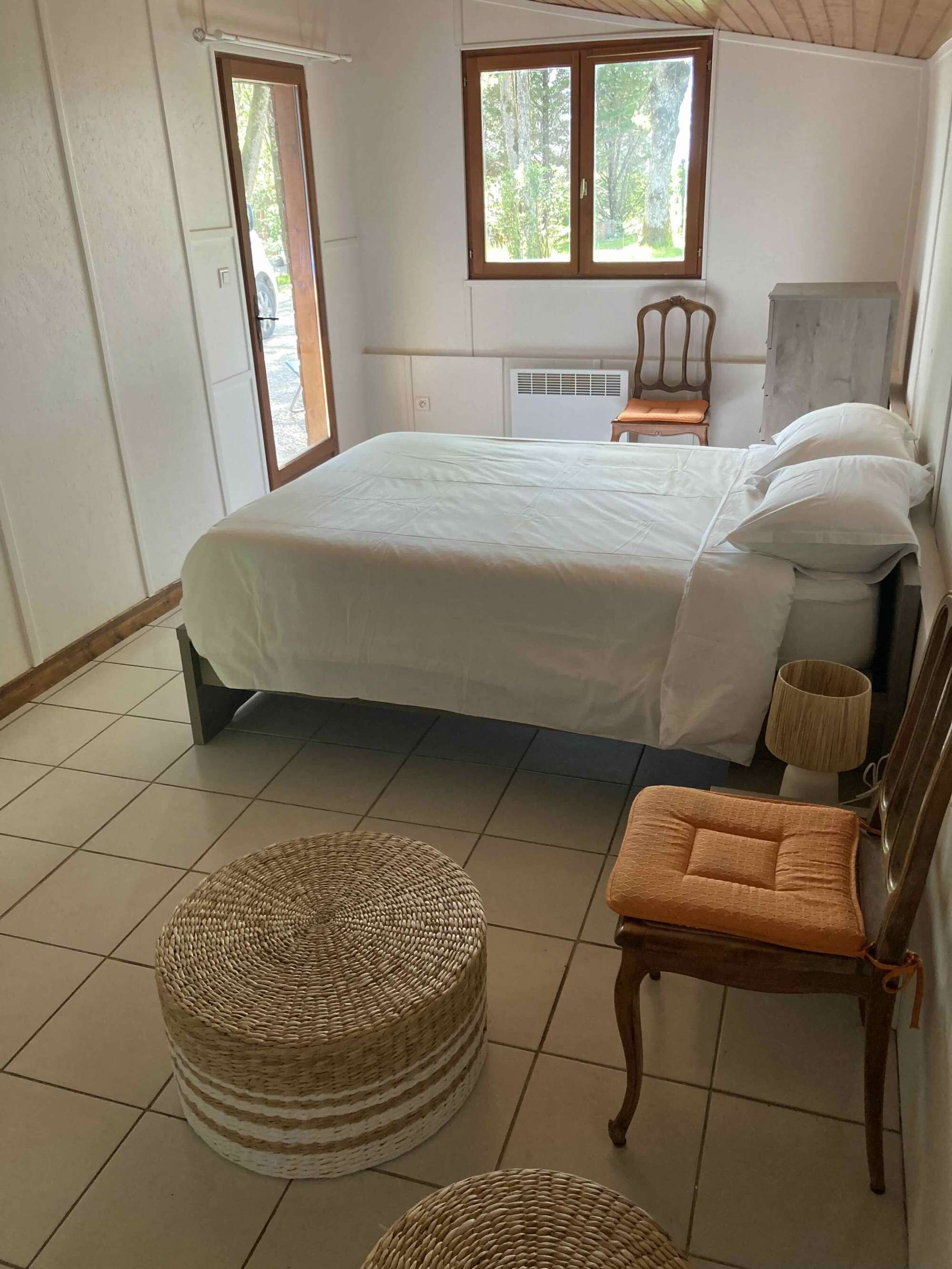 Une chambre à coucher avec un lit, deux chaises, une lampe et une fenêtre.