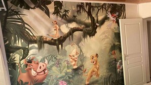 Habitación con un mural en la pared que muestra personajes de la selva animados, una cama y una puerta.