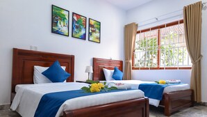 A hotel room with two wooden beds, each with blue and white bedding, and a window with beige curtains. - Hoian Central Garden Homestay (Da Nang)
