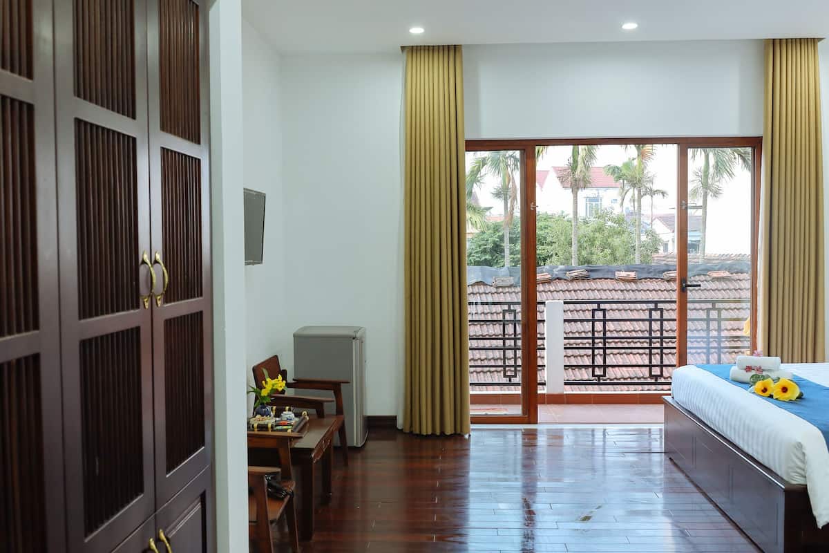 A hotel room with a bed, a desk, a chair, and a view of the outside balcony.