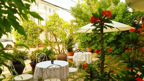 An outdoor patio with white tables and chairs, surrounded by potted plants and flowering plants. - Hoian Central Garden Homestay (Da Nang)