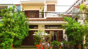 A two-story building with a tiled roof, surrounded by lush greenery and potted plants. - Hoian Central Garden Homestay (Da Nang)