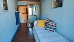Una habitación estrecha con una cama, techo de madera y una puerta que da a otra habitación.