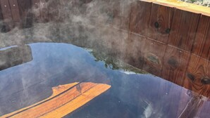 Un bain à remous doté d’une terrasse en bois, entouré de verdure et surplombant un ciel dégagé.