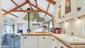Une cuisine avec des armoires blanches, des poutres en bois, un mur en pierre et un plan de travail en bois.