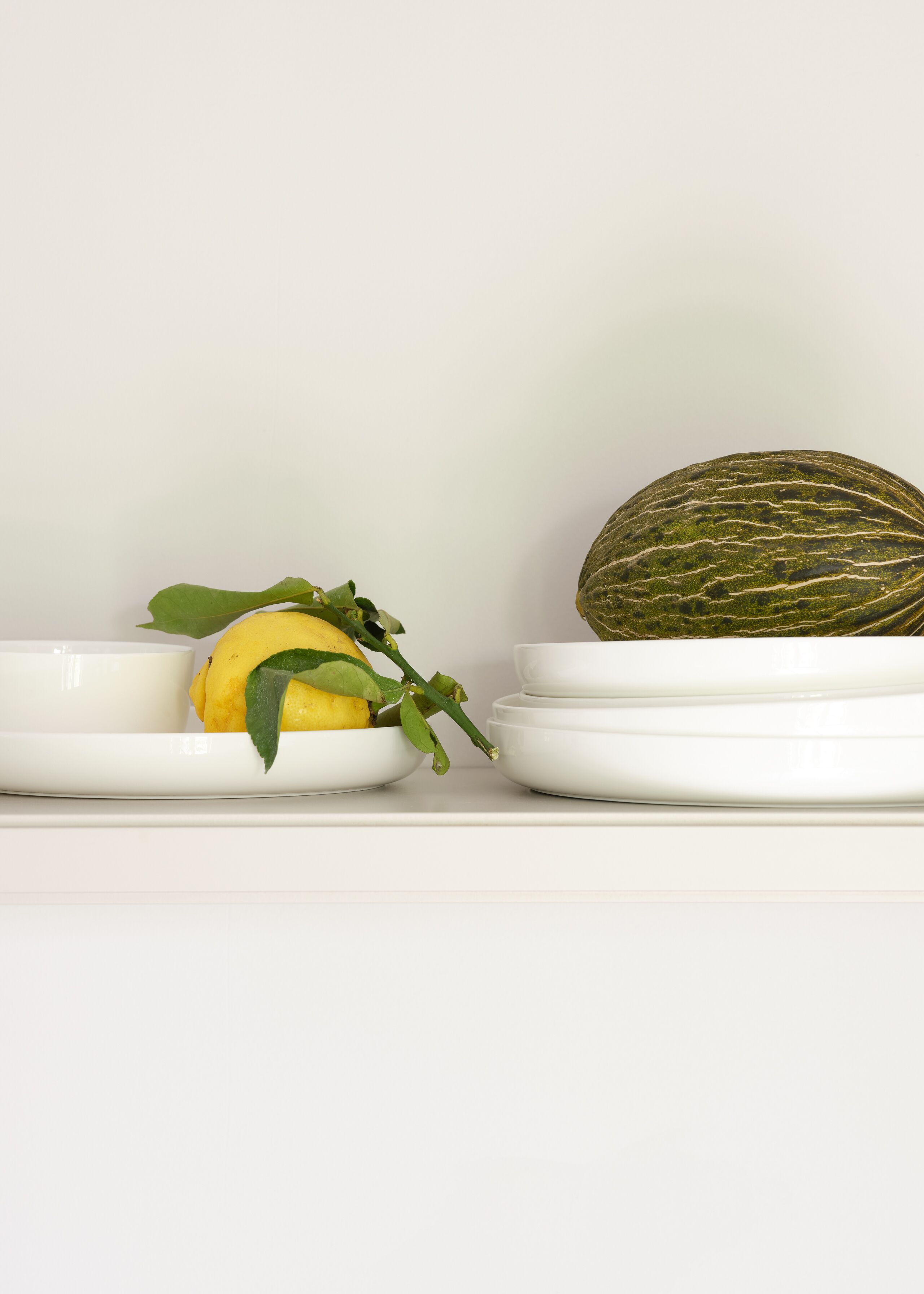 Una estantería blanca con dos cuencos blancos, uno con una fruta amarilla y el otro con un melón verde.