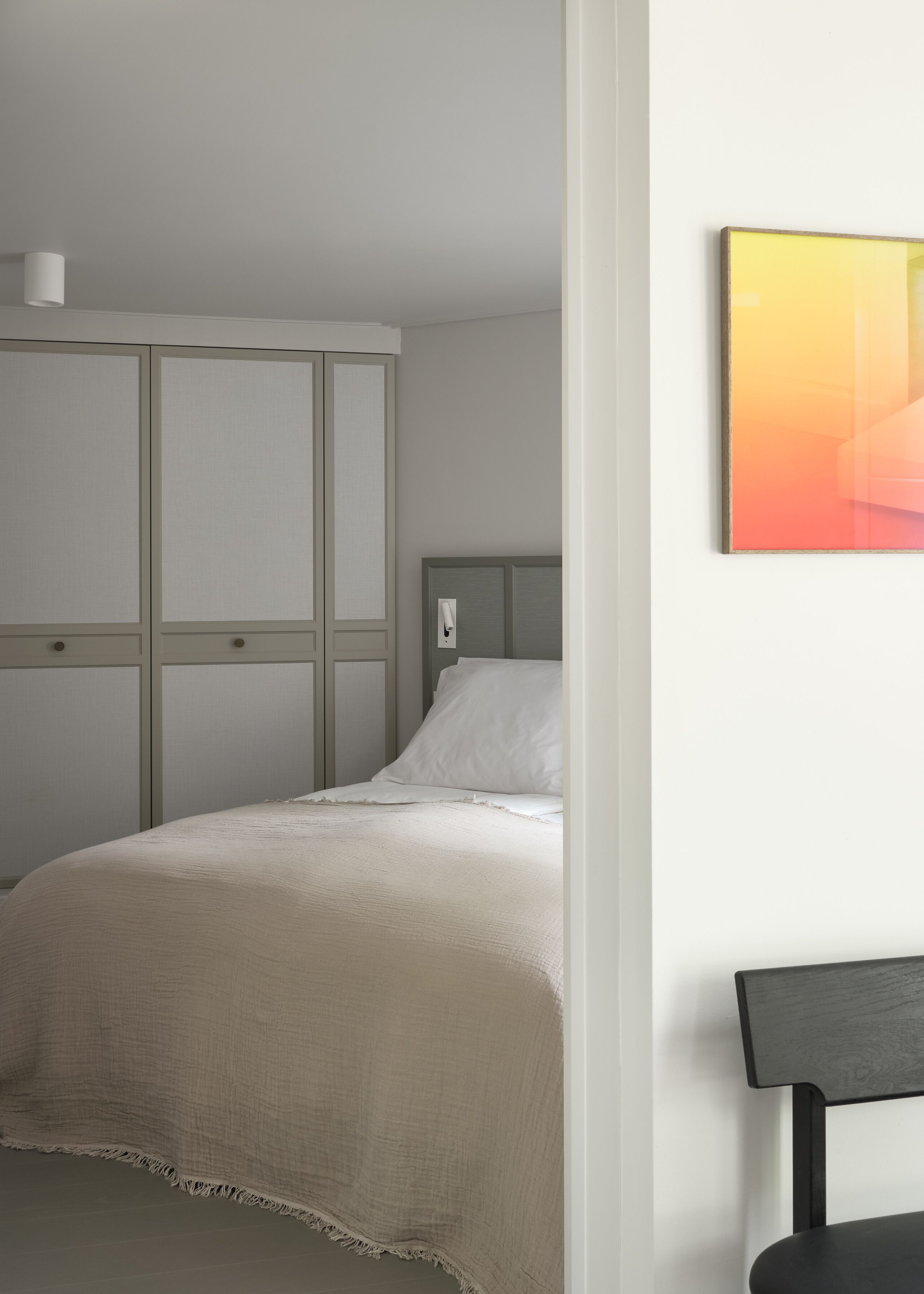 Een slaapkamer met een bed, een nachtkastje, een wandlamp en een lijst met een afbeelding.