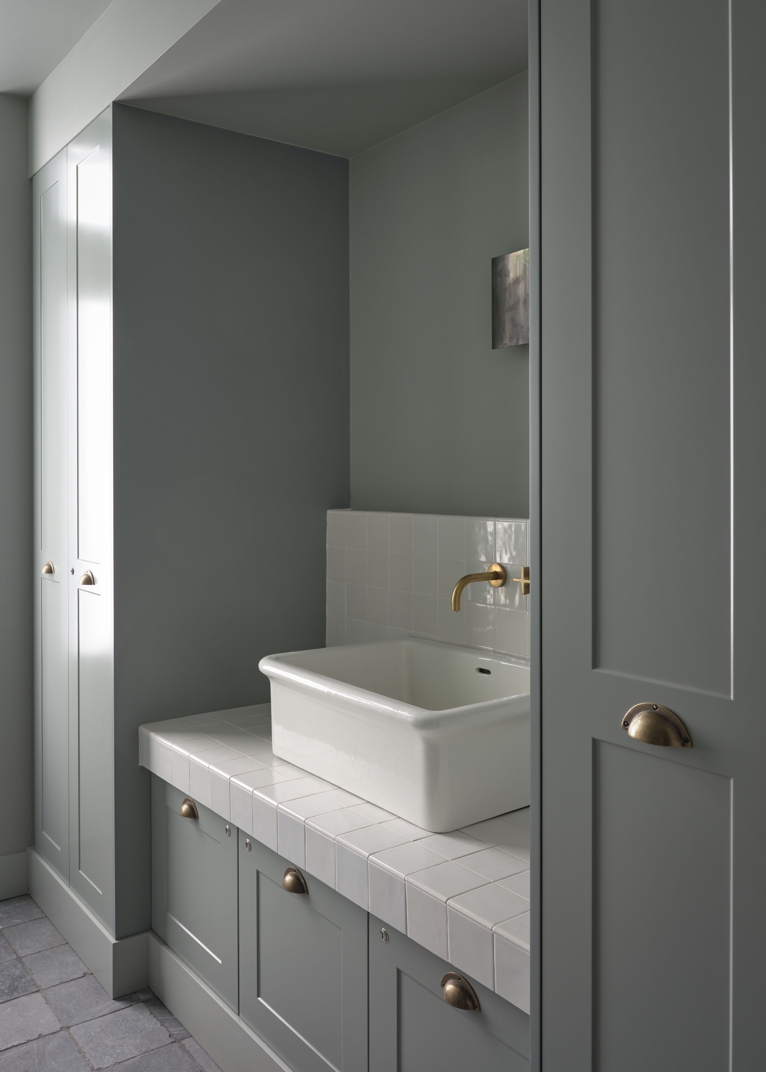 A modern bathroom with a white sink, grey cabinets, and a tiled floor.