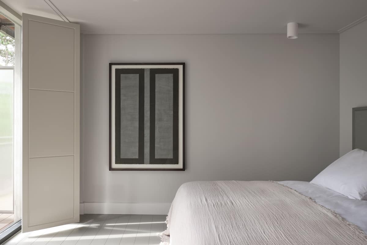 Ein Schlafzimmer mit einem Bett, einem gerahmten Kunstwerk an der Wand und einem Fenster.