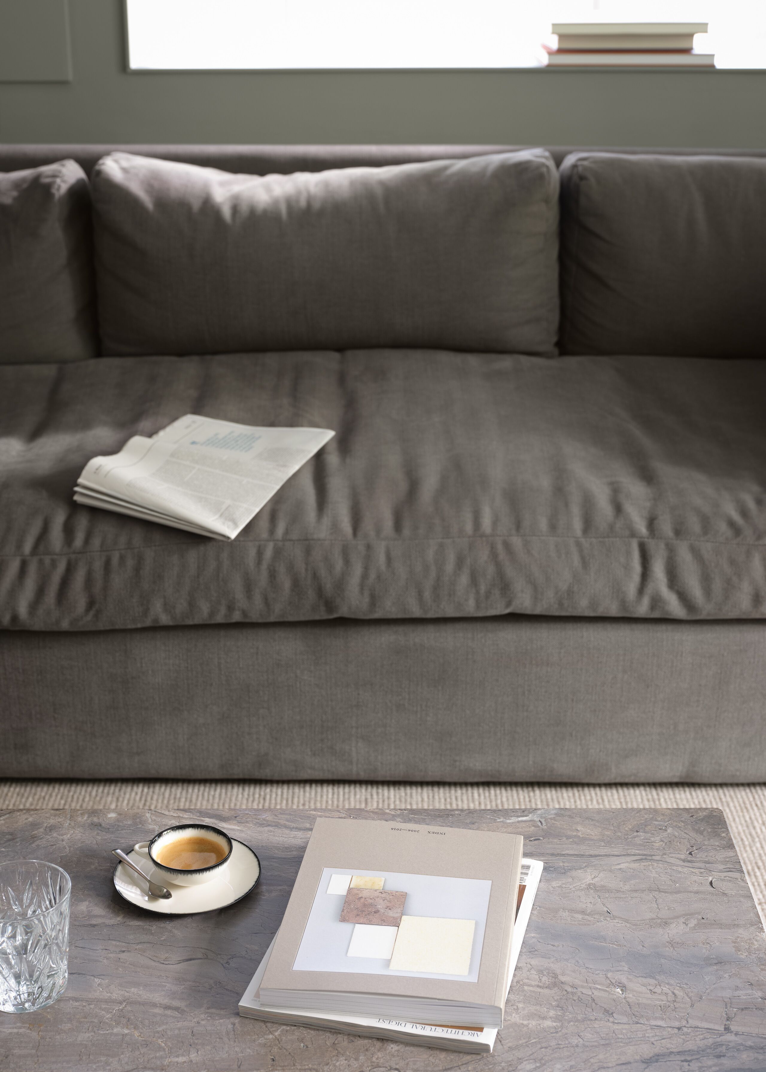 A grey sofa with a newspaper and a coffee cup on a marble table.