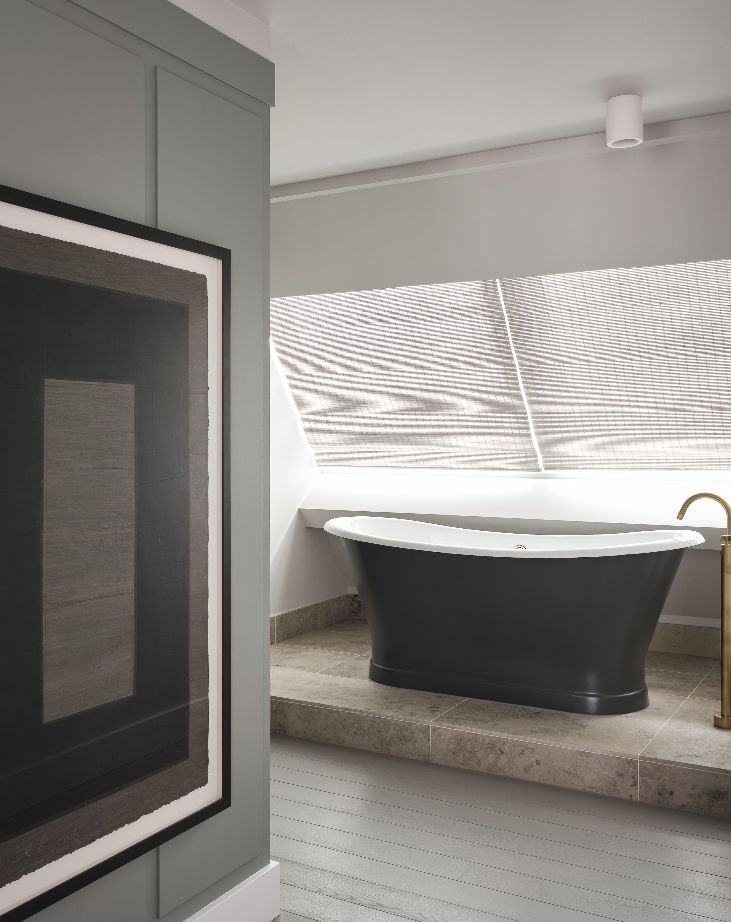 Un baño moderno con una bañera independiente, una obra de arte enmarcada en la pared y un ventanal que proporciona luz natural.