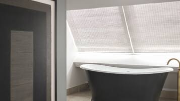 Un baño moderno con una bañera independiente, una obra de arte enmarcada en la pared y un ventanal que proporciona luz natural.