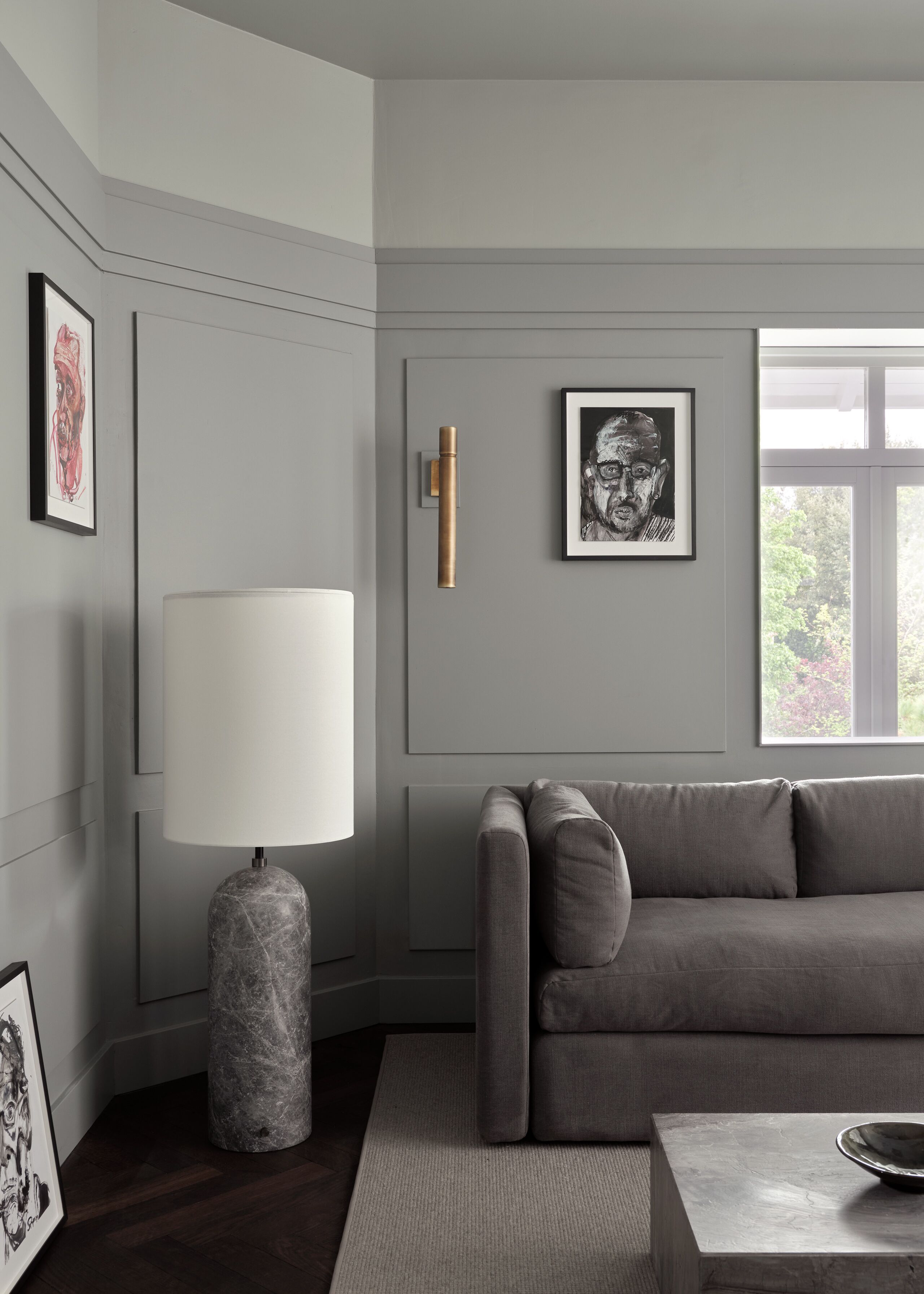 Una sala de estar moderna con un sofá gris, una lámpara de pie de mármol y cuadros en las paredes.