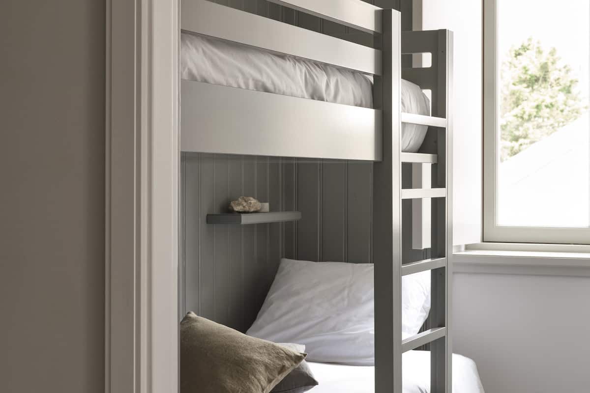 Ein Stockbett mit weißer Bettwäsche, ein Regal mit einem dekorativen Gegenstand und ein Fenster mit Blick auf Grünflächen.