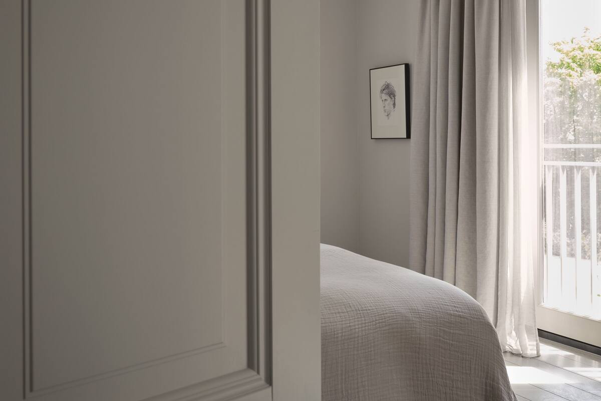 Ein Schlafzimmer mit einem Bett, einem Fenster mit Vorhängen und einem gerahmten Bild an der Wand.