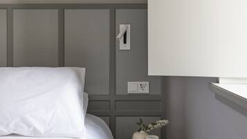 A bedroom with a bed, a small bedside table with a vase, and a wall socket.