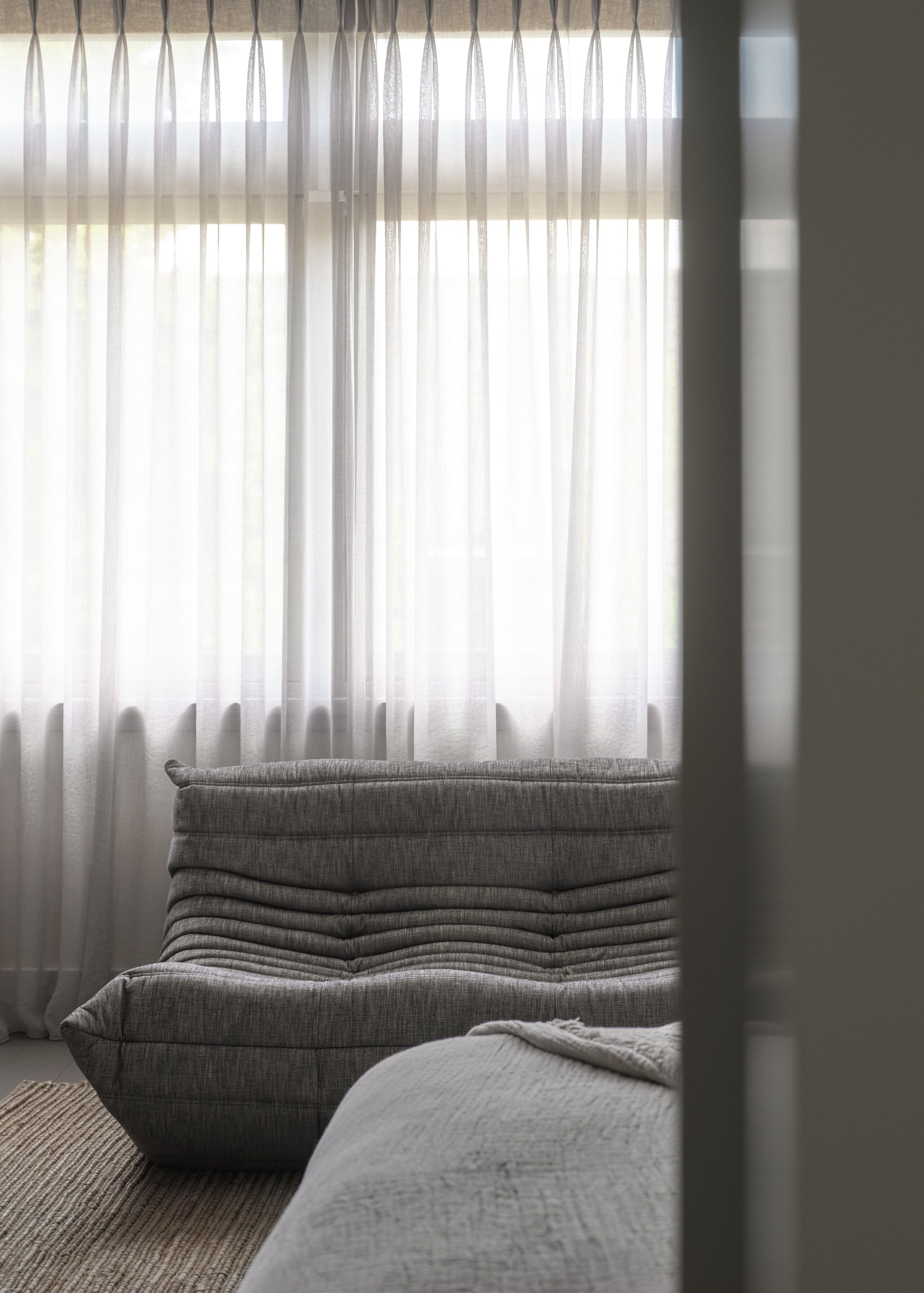 A room with a sofa and a window with sheer curtains.