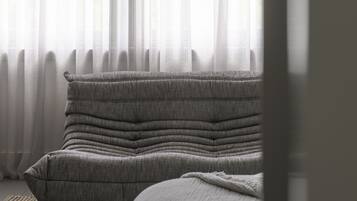 A room with a sofa and a window with sheer curtains.