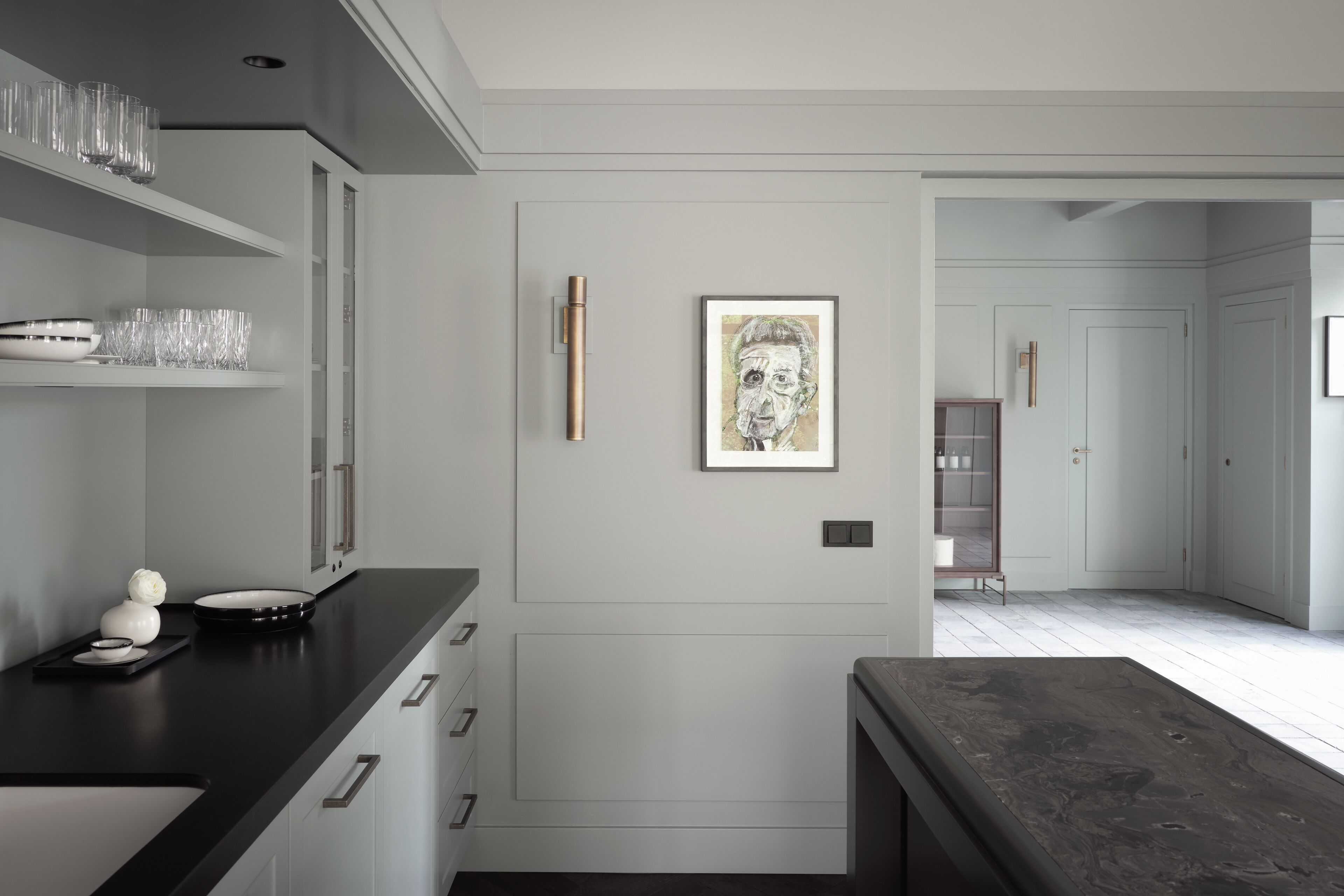 A modern kitchen with white cabinetry, a black countertop, and a framed artwork on the wall.