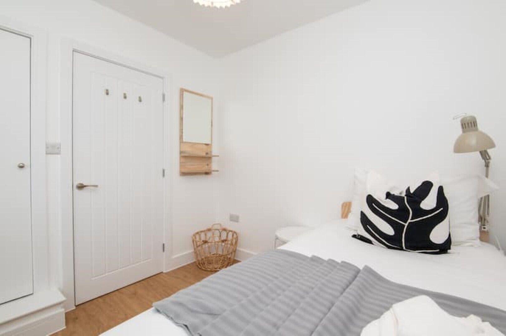 A bedroom with a bed, a bedside lamp, a mirror, and a wicker basket.