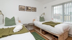 A hotel room with two beds, a small round table, and a window with blinds. - Newly Refurbished Gem | Perfect | Alexa | Sleeps 5 (Bristol)
