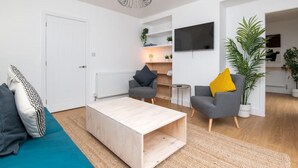 A modern living room with a wooden coffee table, two grey armchairs, a TV mounted on the wall, and a potted plant. - Newly Refurbished Gem | Perfect | Alexa | Sleeps 5 (Bristol)