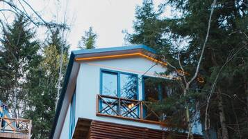 Una cabaña moderna con balcón, rodeada por un bosque frondoso.