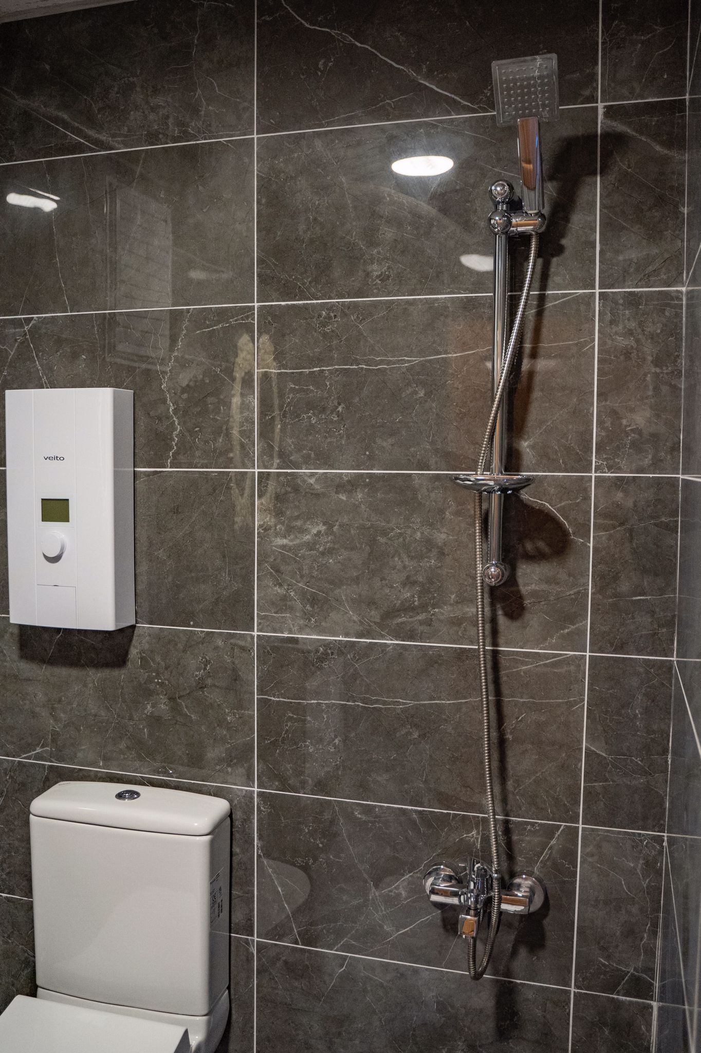 A bathroom with a shower, a toilet, and a hand dryer.