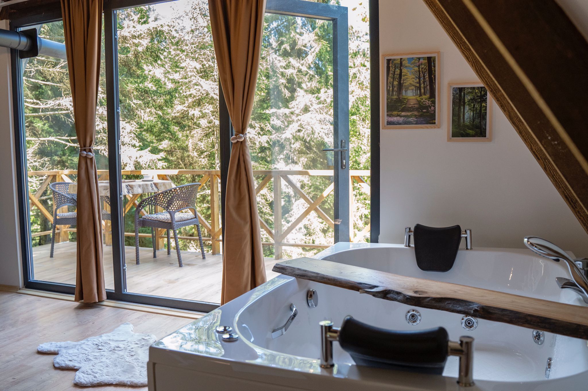 A modern bathroom with a large bathtub, wooden deck outside, and two framed pictures on the wall.
