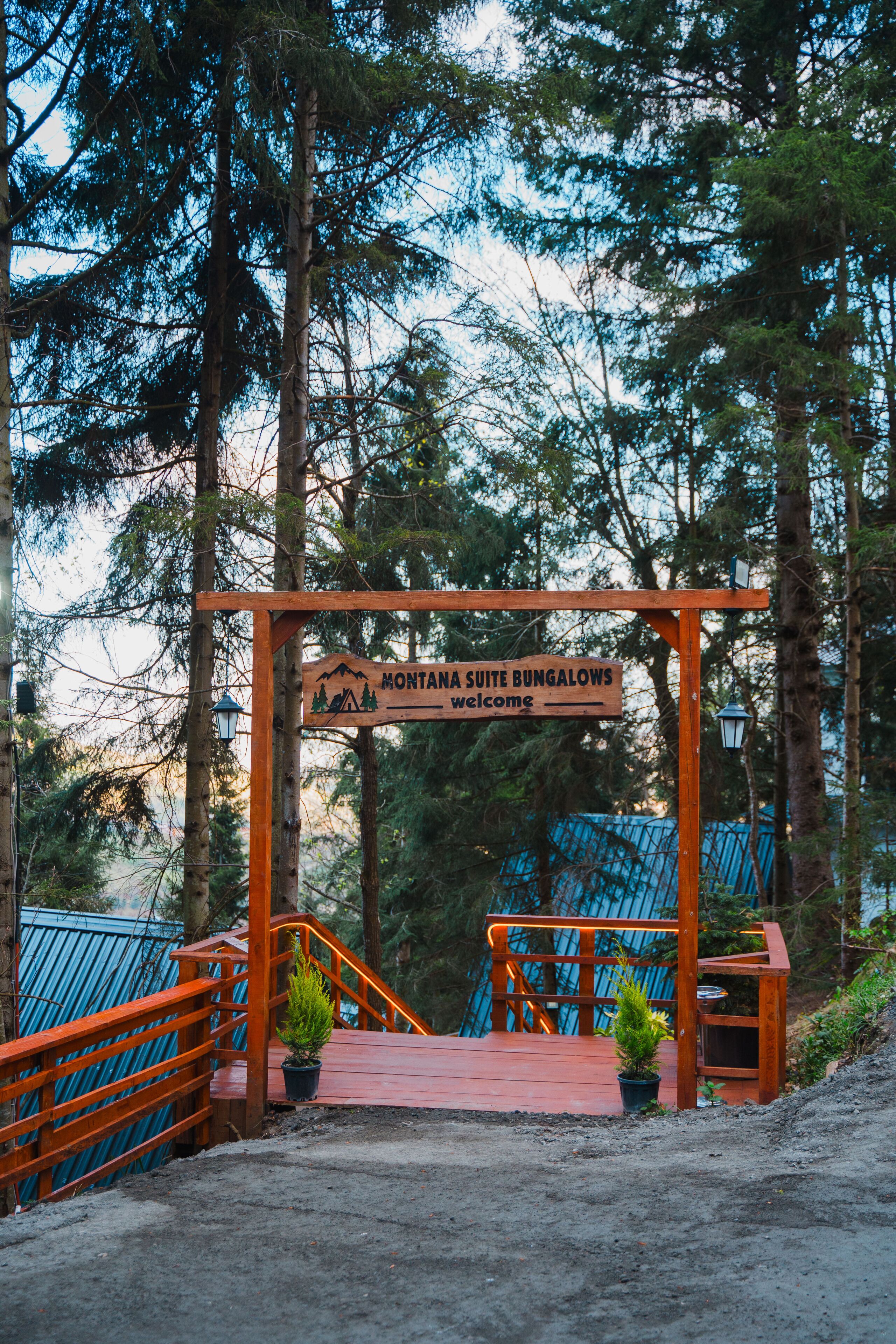 A wooden sign with "Montana Suite Bungalows welcome" written on it, a red staircase, and a blue fence in the background.