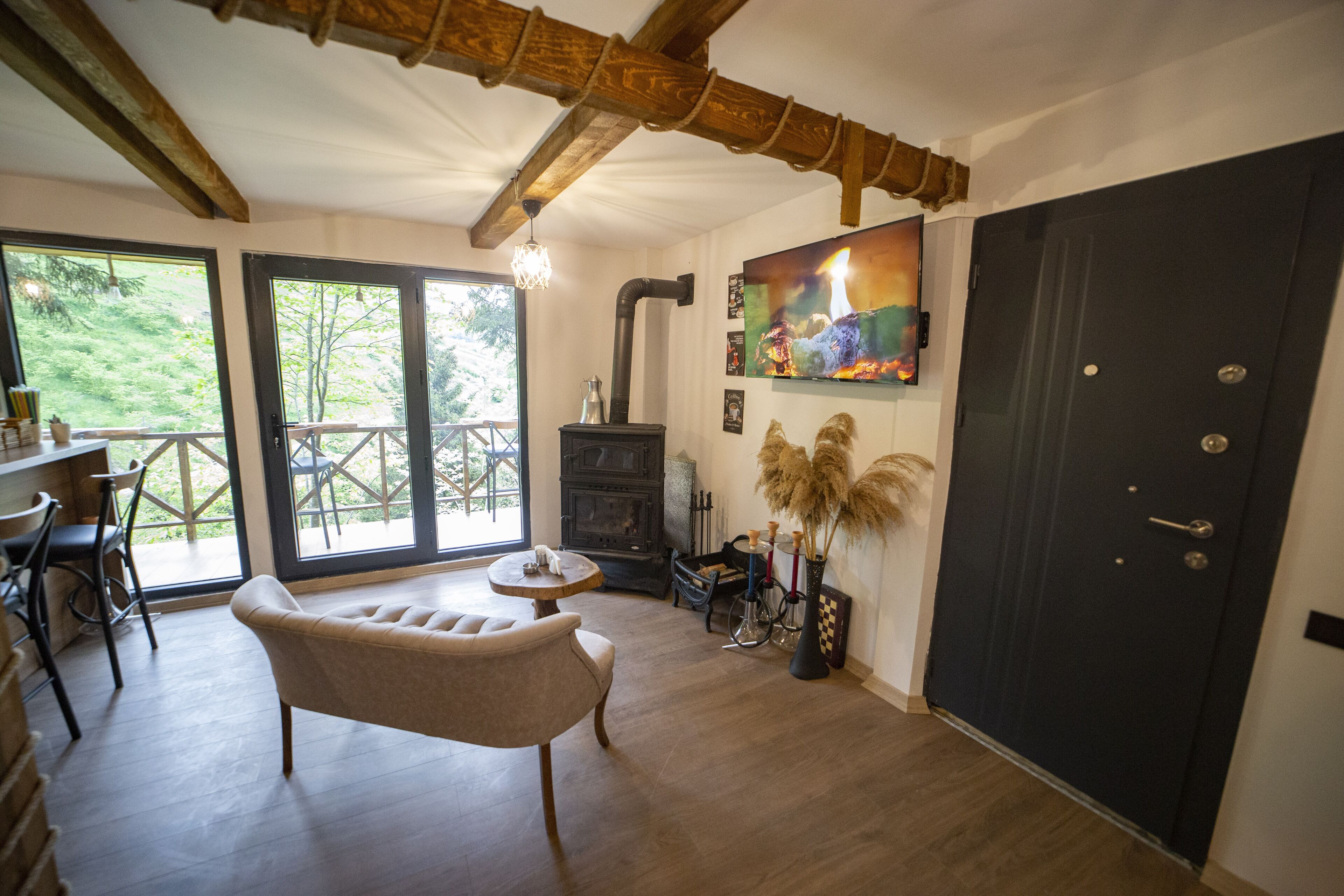 A cozy room with a wooden ceiling, a fireplace, a dining area with chairs, and a large door.