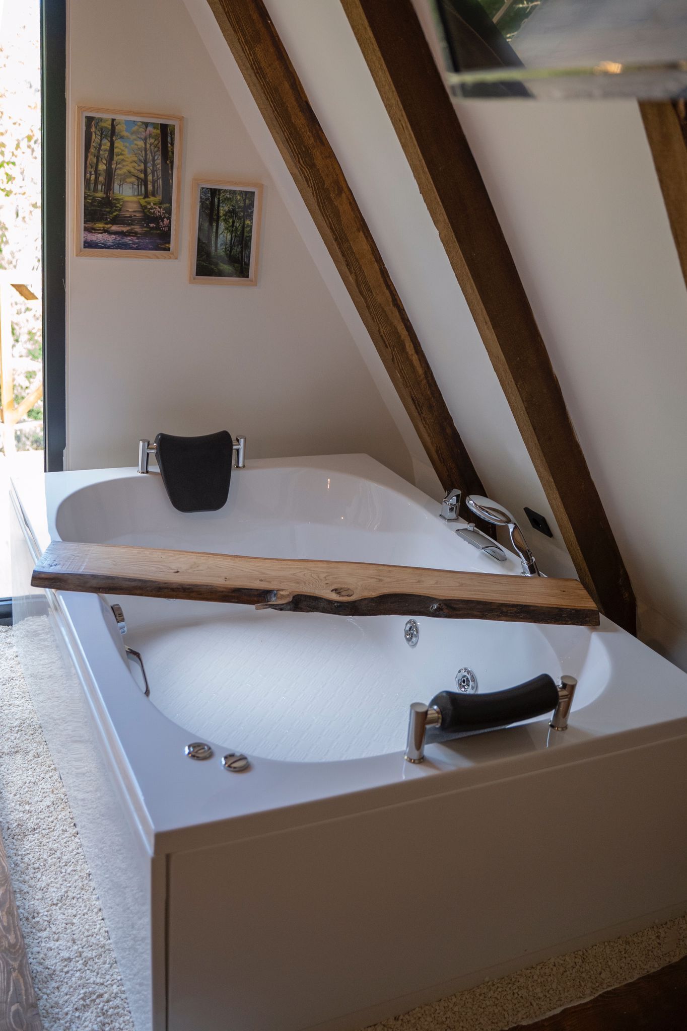 A modern bathroom with a freestanding bathtub, a wooden shelf, and two framed pictures on the wall.