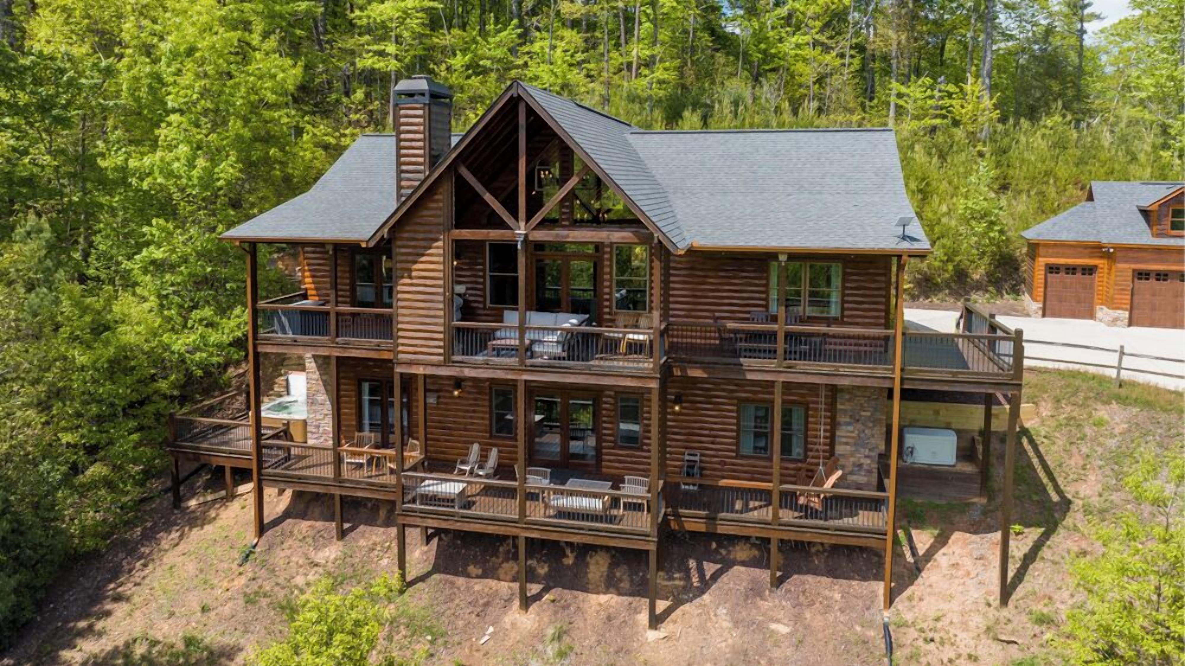 A multi-story log cabin with a balcony on each floor, surrounded by dense forest.