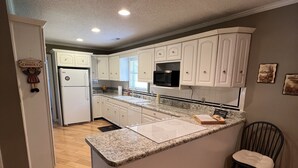 Una cocina moderna con muebles blancos, encimera de granito y microondas integrado.