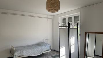A room with a bed, a hanging light fixture, a window with blinds, and a mirror.