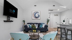 Un salon moderne avec un canapé bleu foncé, deux fauteuils bleu clair, une table basse en verre et un grand tableau abstrait.