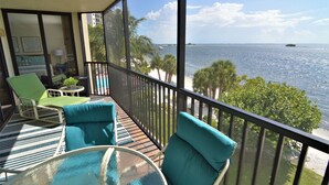 A balcony with a view of the sea, a pool, and a lounge area with chairs and a table.