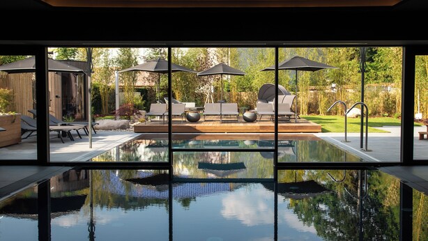 Una piscina con sillas de descanso y sombrillas, rodeada por una terraza de madera y un jardín.