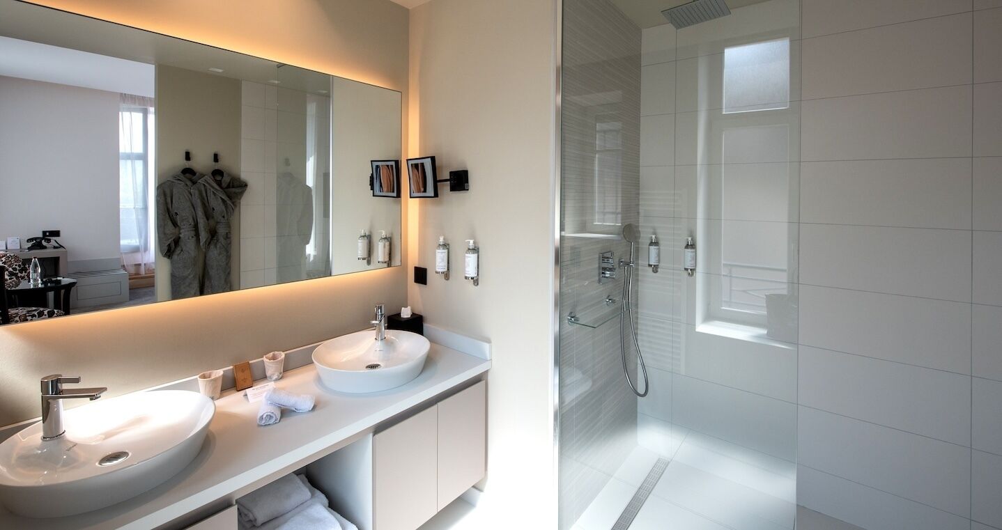 Ein modernes Badezimmer mit einem großen Spiegel, zwei Waschbecken und einer bodenebenen Dusche.