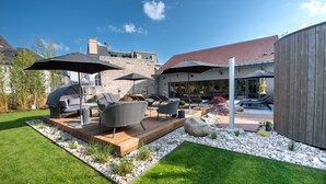 Un patio con mobiliario exterior, sombrillas y una pared de piedra al fondo.