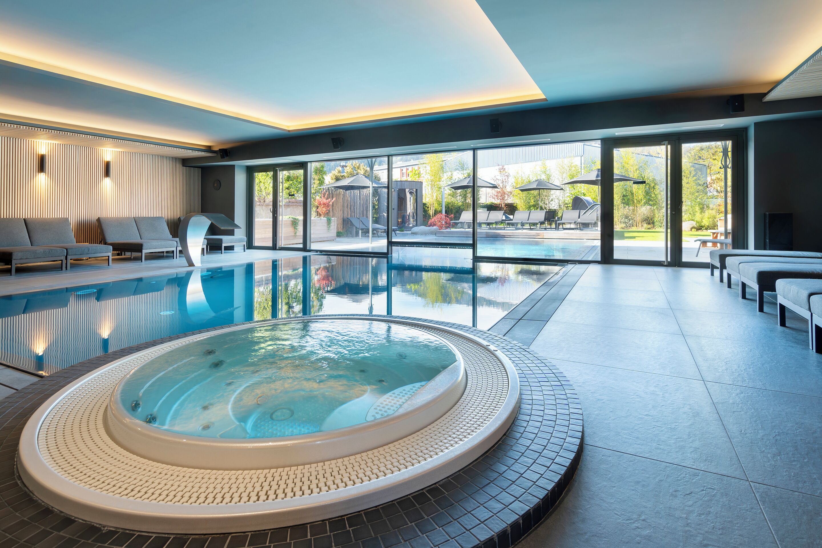 Piscina interior moderna com hidromassagem, espreguiçadeiras e vista para a área externa.
