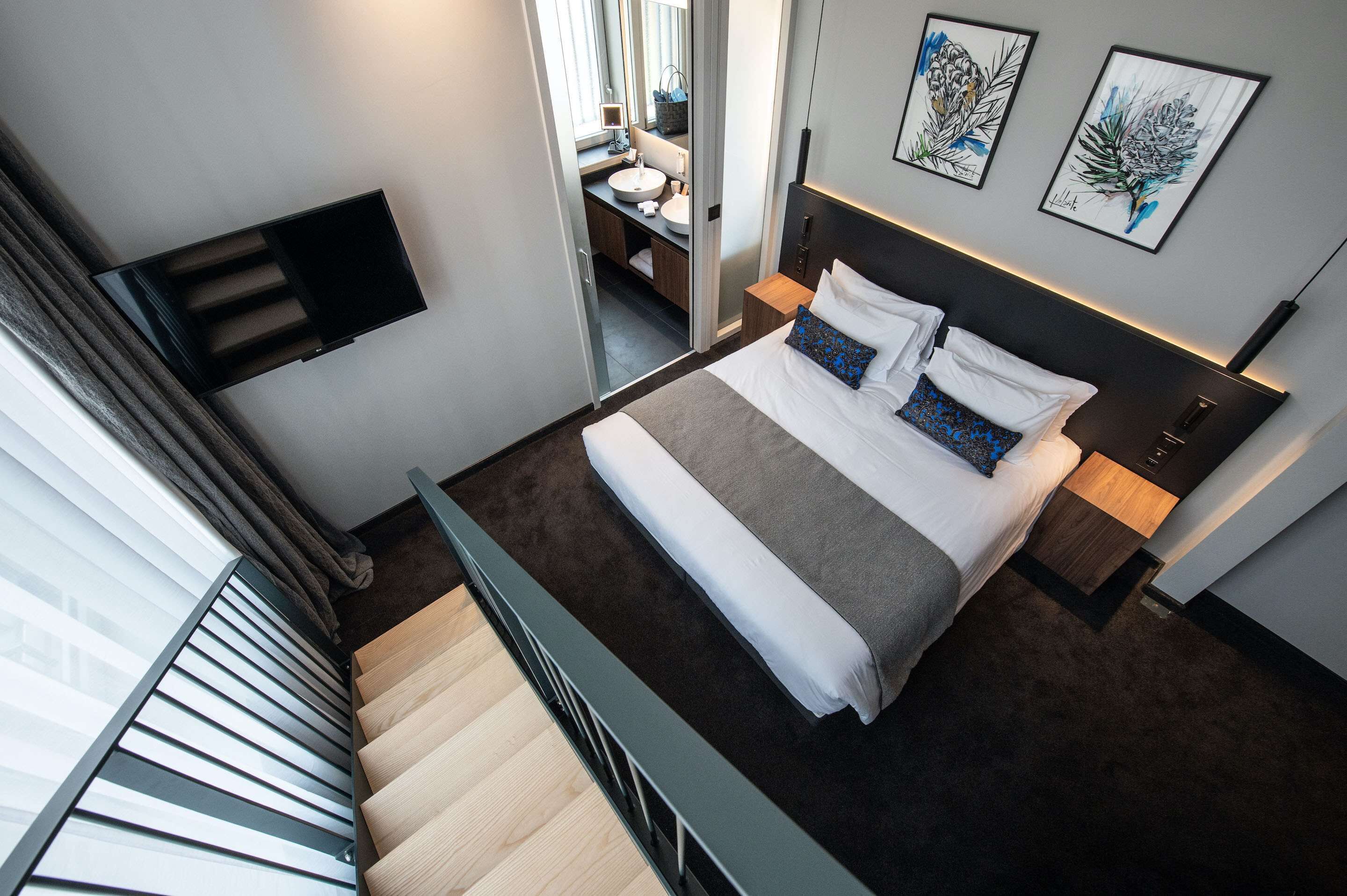 Une chambre d’hôtel moderne équipée d’un lit, d’une table de chevet et d’un téléviseur fixé au mur.