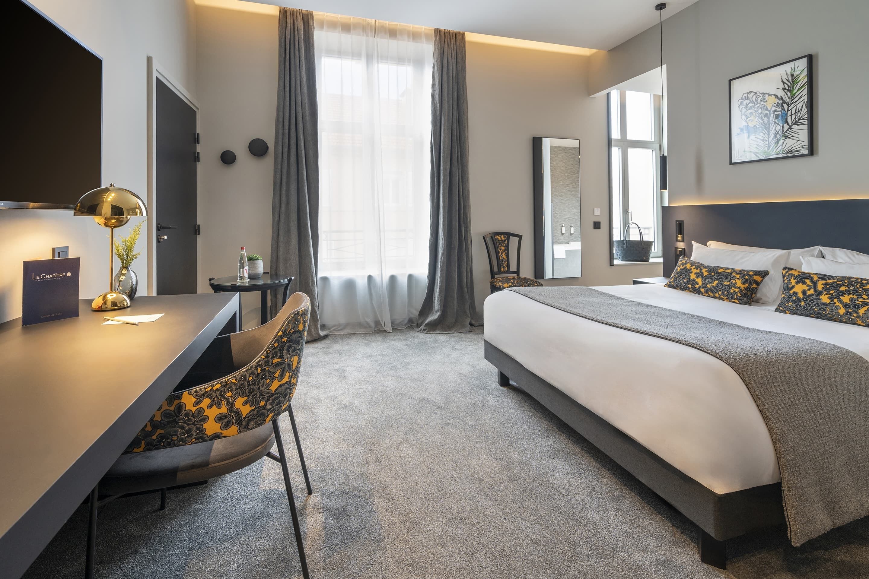 Een hotelkamer met een bed, een bureau, een stoel en een groot raam met gordijnen.