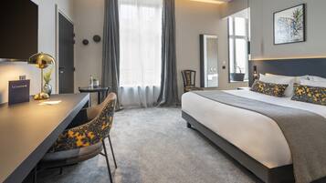 Een hotelkamer met een bed, een bureau, een stoel en een groot raam met gordijnen.
