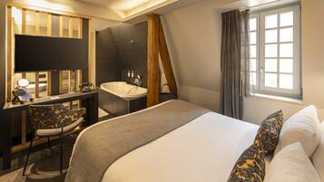 Una habitación de hotel moderna con una cama grande, un escritorio con una silla, una bañera y un ventanal con cortinas.