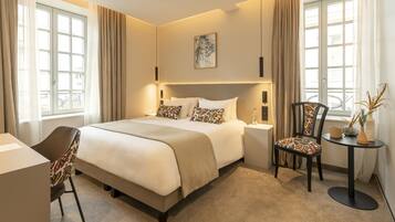A hotel room with a bed, a desk, a chair, a small table, and a window with curtains.