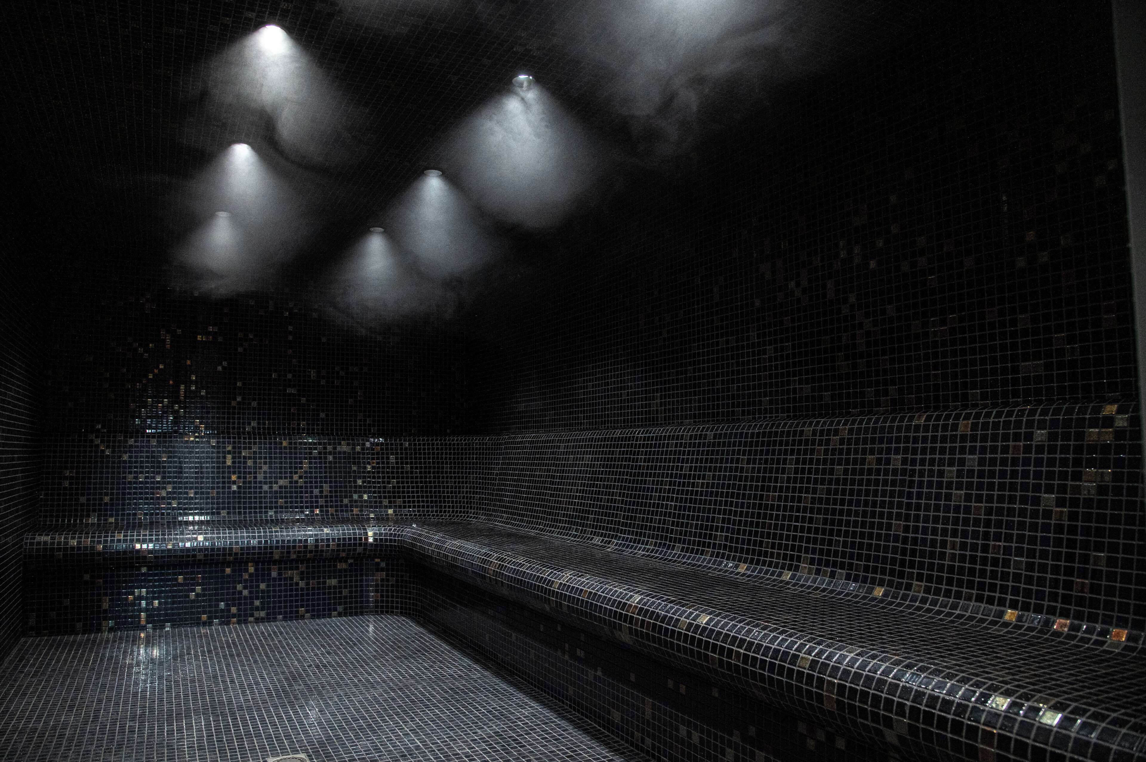 A dark, tiled interior with a bench and a wall of small, square tiles.