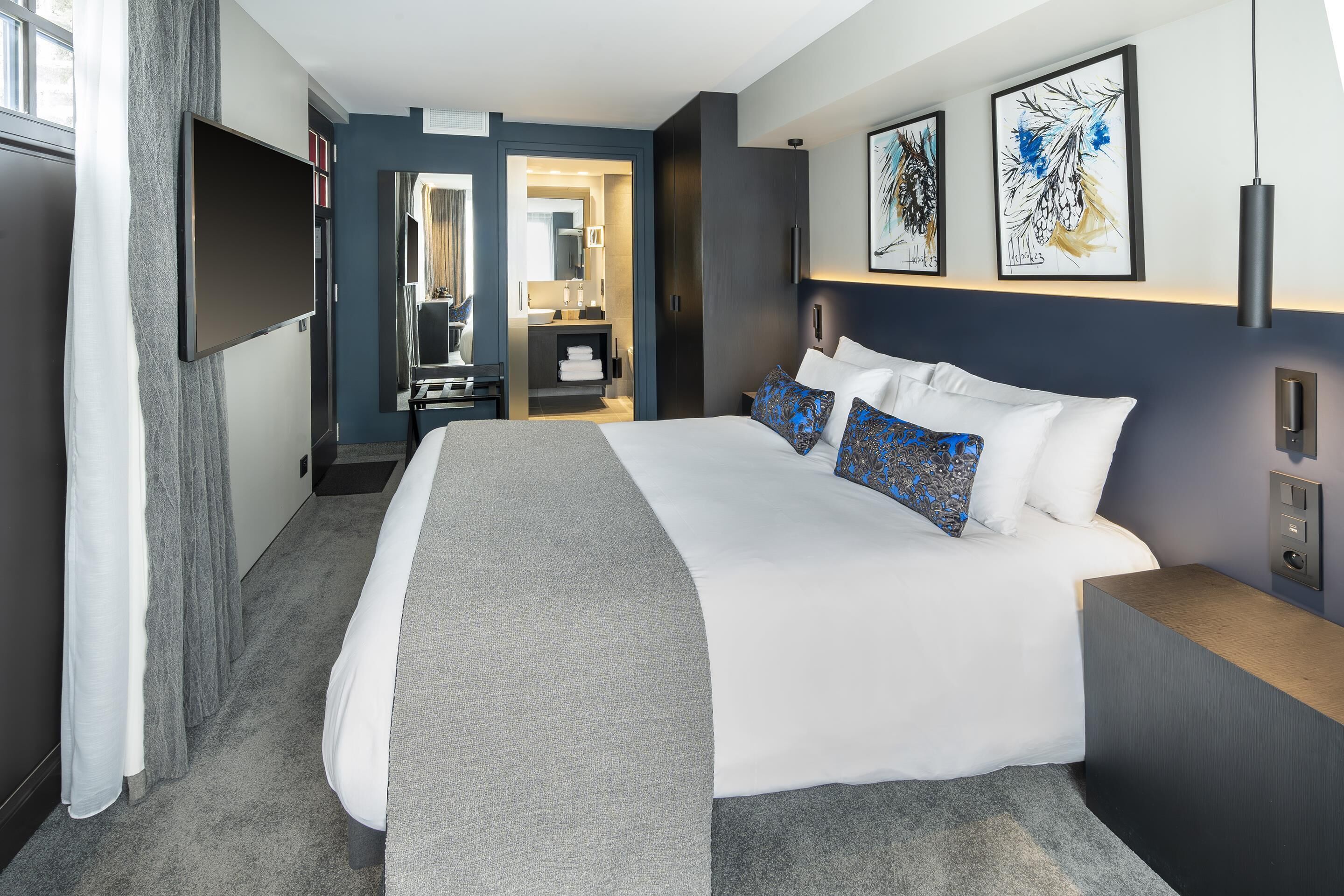 Quarto de hotel com uma cama grande, televisão de tela plana, escrivaninha e obras de arte na parede.