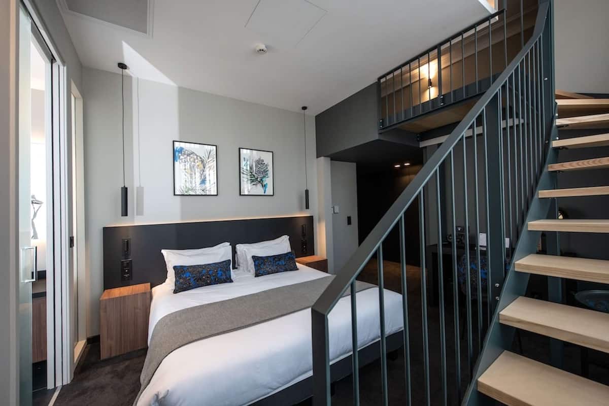 Una habitación de hotel moderna con una cama grande, una escalera y obras de arte en las paredes.