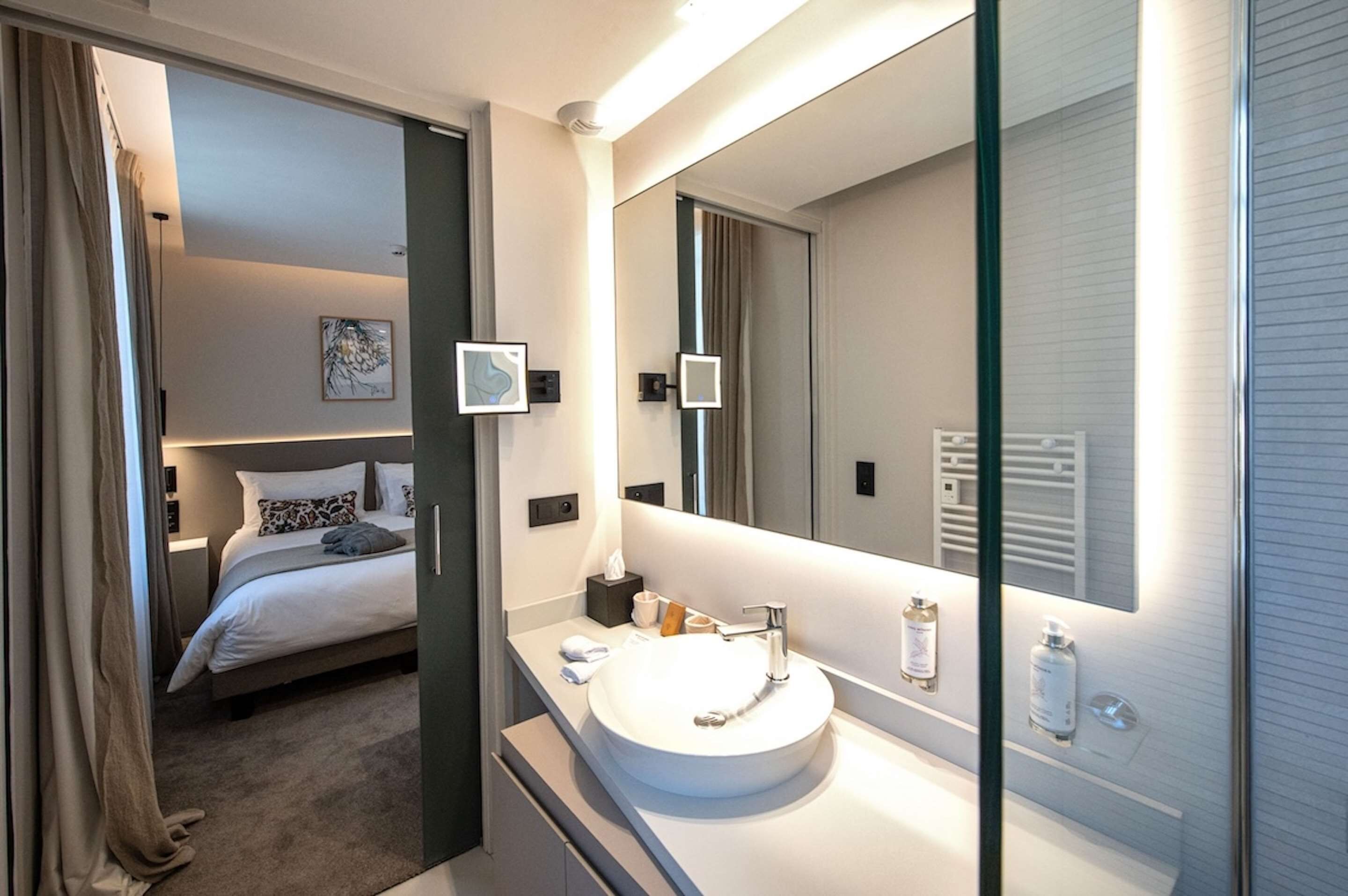 A modern hotel room with a large bed, a round white sink, and a large mirror.
